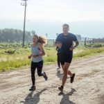 Group of joggers running along a rural dirt path surrounded by nature.